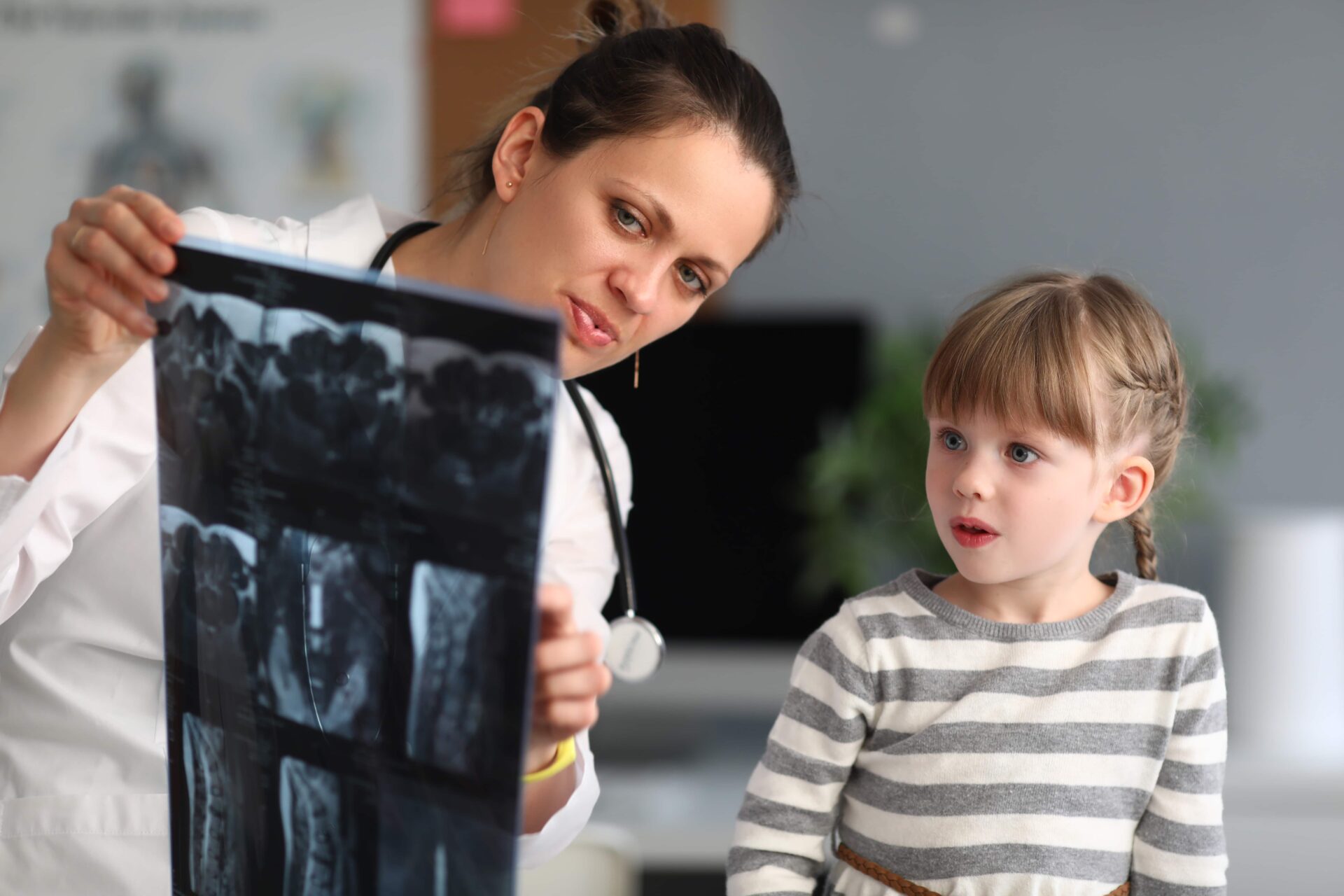 Woman doctor shows child patient an xray in clinic. Use of radiation diagnostics of diseases of skeletal system in pediatric practice concept.