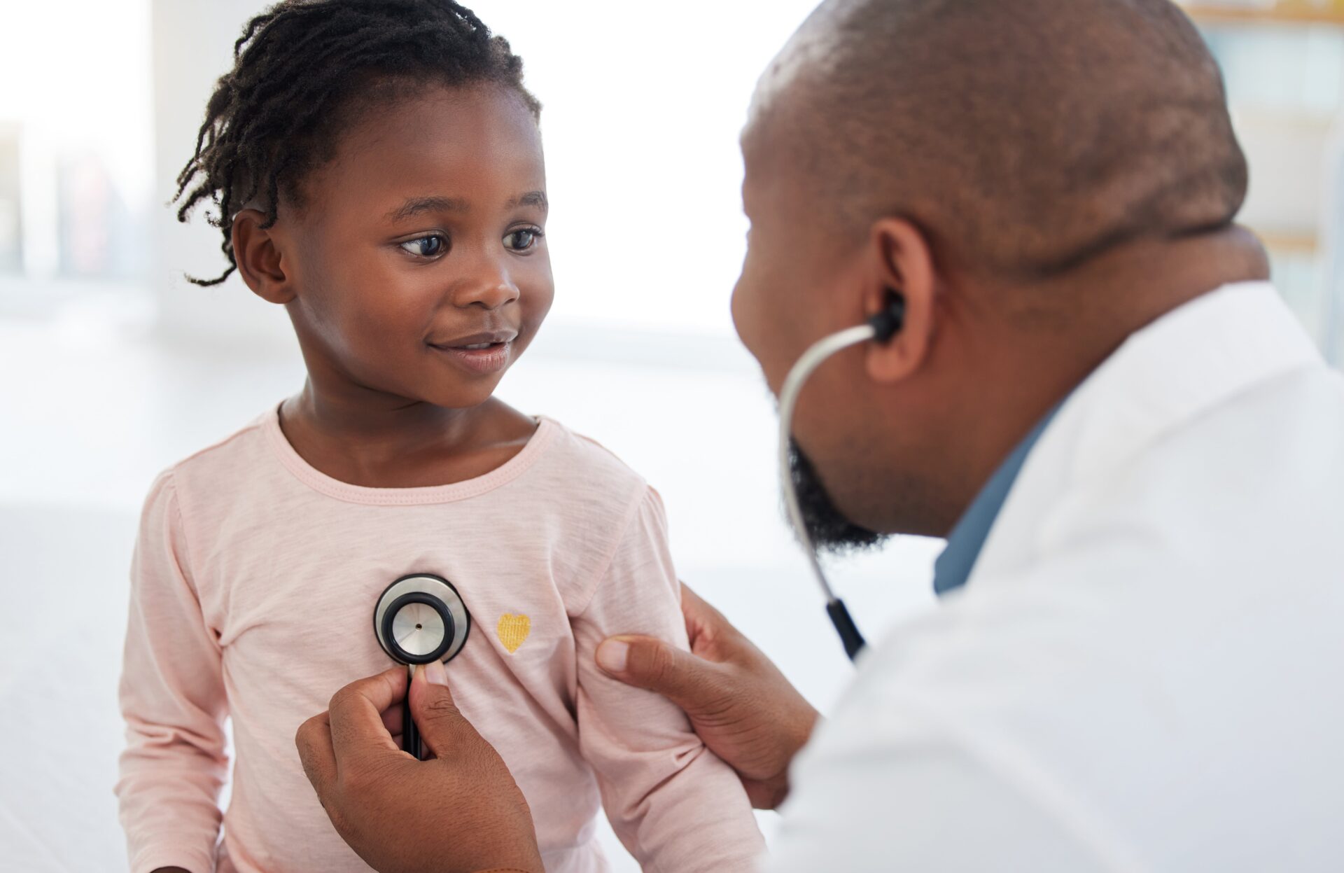 Healthcare, pediatrician and child heart doctor with a patient at hospital, exam on chest with a stethoscope. Black girl smile at pediatric surgeon, talking to a friendly, caring physician she trust.